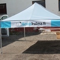 Harmaa 3x4,5m popup teltta, jonka katon reunalle on kiinnitetty tarranauhoilla pvc banneri