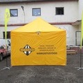 4x4m kollane popup telk logodega seintel ja katuse äärtes. 4m RM lipud ristjalaga